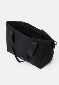 Sac fourre-tout noir en tissu durable, avec deux poignées, une fermeture zippée et un intérieur spacieux doté de poches. Texture lisse, design minimaliste.