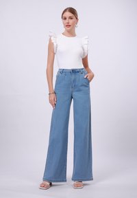 Bel črtast zgornji del z ruffled rokavi v kombinaciji z visokim pasom, širokimi svetlo modrimi džinsom in belimi s sandali z naramnicami.