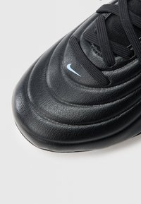 Μαύρο δερμάτινο αθλητικό παπούτσι με καμπυλωτή υφή και ραμμένα σχέδια, με μαύρα κορδόνια και μικρό ανοιχτό μπλε λογότυπο Nike στο πλάι.