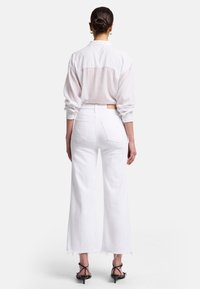 Camicia bianca oversize con maniche lunghe e tessuto leggero e trasparente, abbinata a jeans bianchi a vita alta con gamba larga e orli sfilacciati.