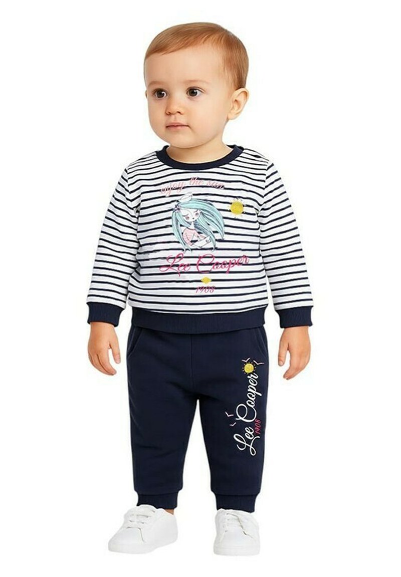 Tenue pour tout-petit comprenant un haut à manches longues rayé bleu marine et blanc avec un imprimé graphique, associé à un pantalon bleu marine et des baskets blanches.