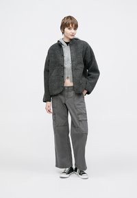 Γκρι φλις μπουφάν με κουτί σχήμα, κουμπιά κλεισίματος και πλαϊνές τσέπες, φορεμένο πάνω από ένα ανοιχτό γκρι cropped φούτερ και γκρι παντελόνια cargo.