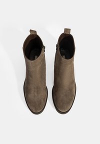 Paire de bottines en daim marron avec fermetures éclair latérales et languettes, vues de dessus sur fond blanc.