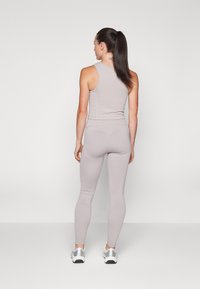 Világosszürke sportos öltözet ujjatlan toppal és testhez simuló leggingssel. Simaszerű anyagtextúra, minimalista design ezüst tornacipővel párosítva.