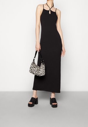 Vestido maxi negro ajustado con tirantes finos y un detalle de ojal. Combinado con un bolso de estampado de cebra y sandalias de tacón grueso.
