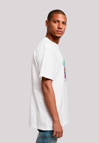 White cotton T-shirt with a colorful splash graphic on the front, featuring a loose fit and short sleeves, worn with blue denim jeans.