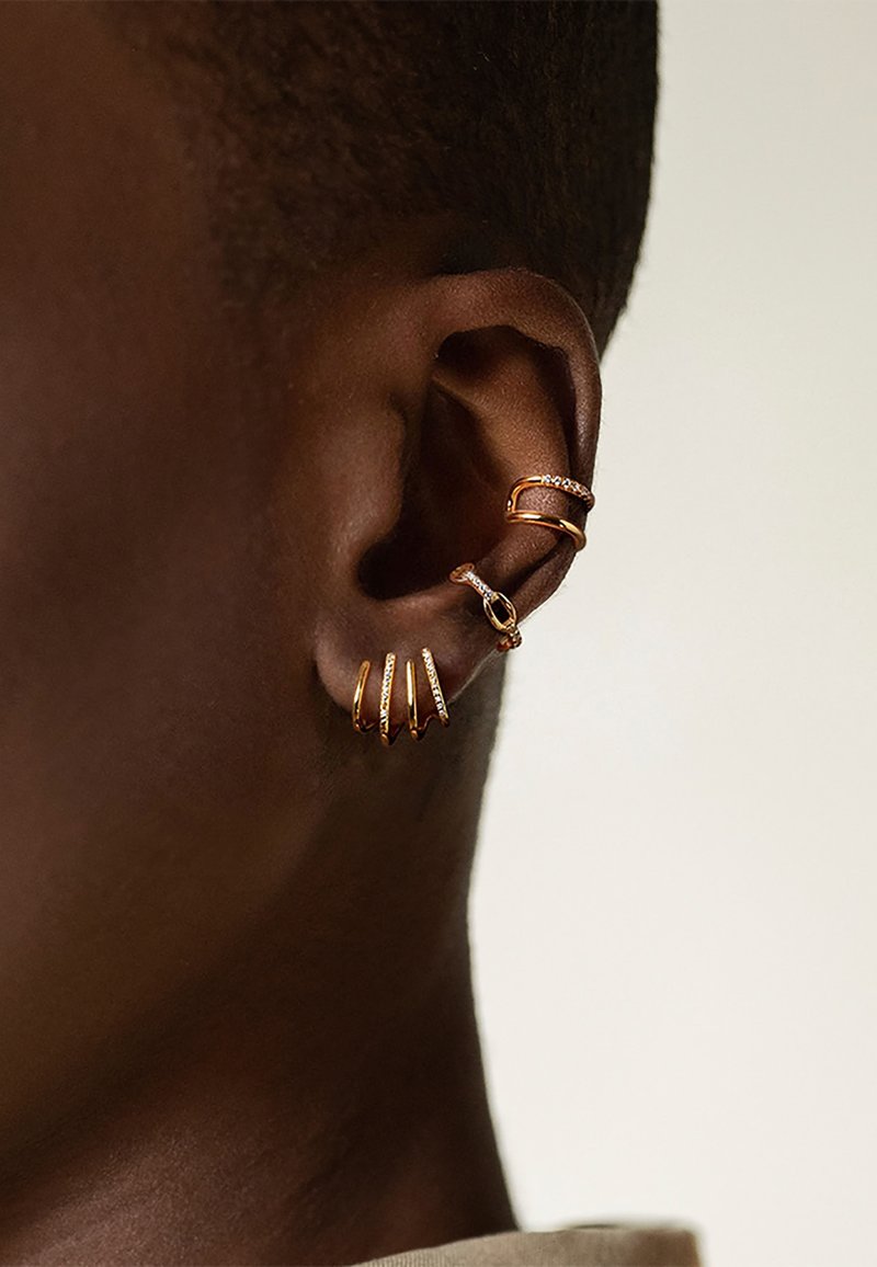 Gold-tone ear cuff featuring several minimalist designs, including curved bands and textured accents, set against a dark skin tone.