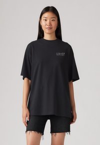 T-shirt en coton noir surdimensionné à manches courtes, présentant un petit logo blanc Levi's sur la poitrine. Porté avec un short en denim noir.