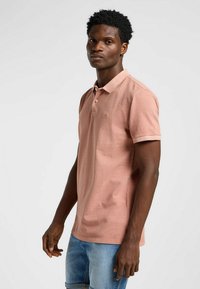 Ljusrosa polo skjorta i mjukt tyg, med klassisk krage, tvåknäppning och korta ärmar, tillsammans med denimshorts.