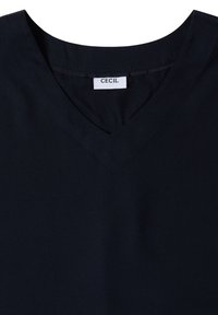 T-shirt noir à col en V avec une étiquette blanche cousue affichant le nom de la marque "CECIL" au col.