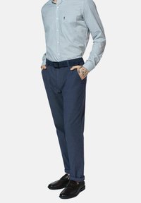 Koszula w niebiesko-białą kratę, zapinana na guziki, w połączeniu z granatowymi spodniami i czarnymi butami. Koszula ma długie rękawy i dopasowany krój.