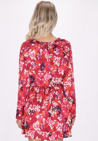 Rochie roșie cu flori, cu mâneci lungi, având un gât elastic și talie elastică, afișând un model vibrant în nuanțe de roz, alb și negru.