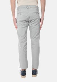 Pantaloni in cotone grigi con vestibilità slim, tasche posteriori visibili e una texture liscia. Abbinati a scarpe scure e una camicia chiara.