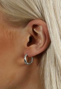 Söljörhänge med en slät, polerad yta, cirkulär design och en lätt kurva, visat på ett mänskligt öra.