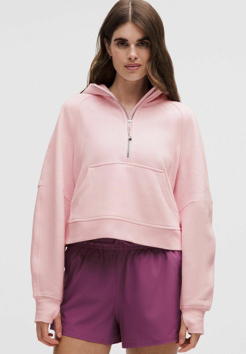 Rosa geschnittenes Hoodie mit einem Viertel-Reißverschluss, Vordertasche, weicher Textur und lockeren Ärmeln, kombiniert mit lila Sportshorts.