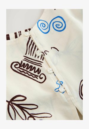 Gros plan sur un tissu crème avec une couture boutonnée et un art linéaire abstrait bleu et marron comprenant des spirales, des colonnes et des formes de feuilles.