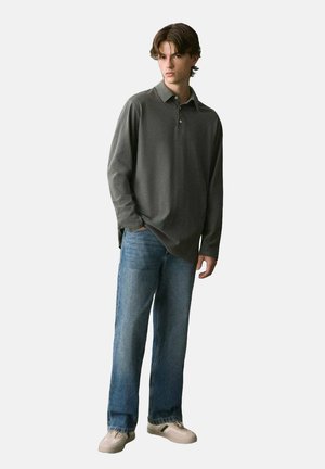 Camisa de polo gris de manga larga con cuello, combinada con jeans de mezclilla azul claro y zapatos beige con franjas verdes.