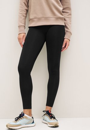 Sorte leggings med en glat tekstur, parret med en lysebrun sweatshirt og blå, beige og marineblå sneakers.