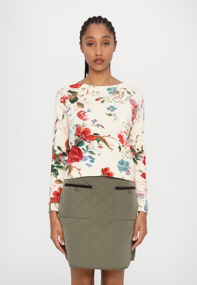 Pull en maille à motif floral crème avec des accents rouges et bleus, associé à une jupe matelassée verte olive avec deux poches avant.