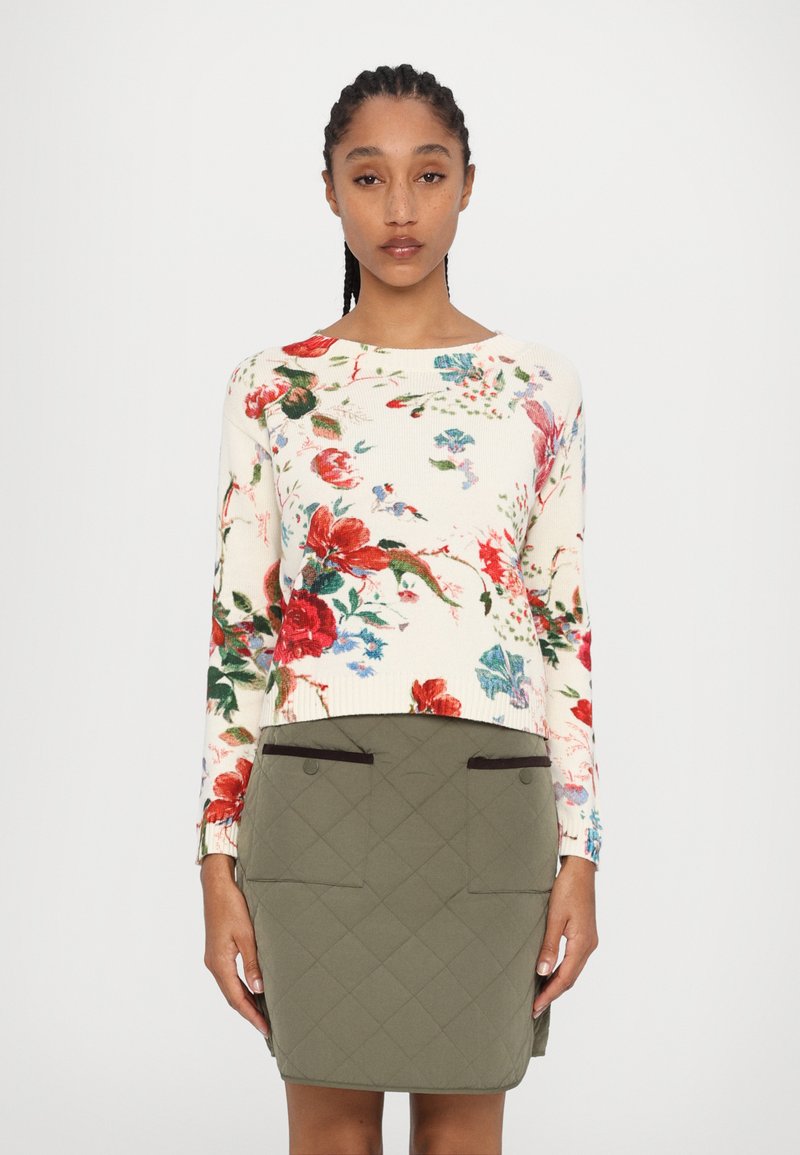 Pull en maille à motif floral crème avec des accents rouges et bleus, associé à une jupe matelassée verte olive avec deux poches avant.