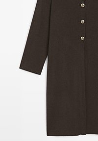 Manteau marron en mélange de laine avec une coupe droite, manches 3/4, et cinq boutons métalliques sur le devant. Texture lisse, design minimaliste.