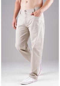 Beige Baumwoll-Chinos mit geradem Bein, ausgestattet mit Fronttaschen und einem Reißverschluss. Kombiniert mit weißen Sneakers.