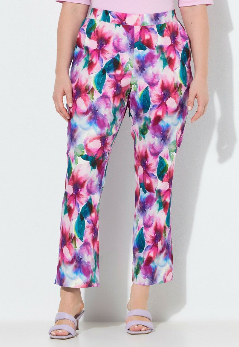 Mujer vistiendo pantalones de pierna ancha con estampado floral de colores brillantes rosa, morado, verde y azul, combinados con sandalias de tacón color lila claro.