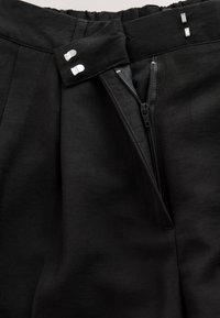 Pantaloni negri cu fermoar parțial deschis și două închizători metalice cu cârlig și bară în talie.
