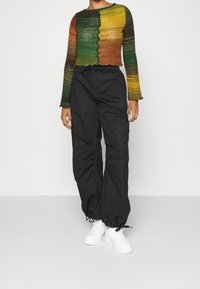 Flerfärgad kort tröja med utställda ärmar i gröna, orange och gula nyanser; kombinerad med svarta cargobyxor och vita sneakers.