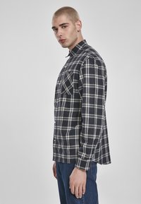 Mørk rutete skjorte med hvit sjekkemønster, knapp-down krage, lange ermer og sidesplitter, sammen med blå denim jeans.