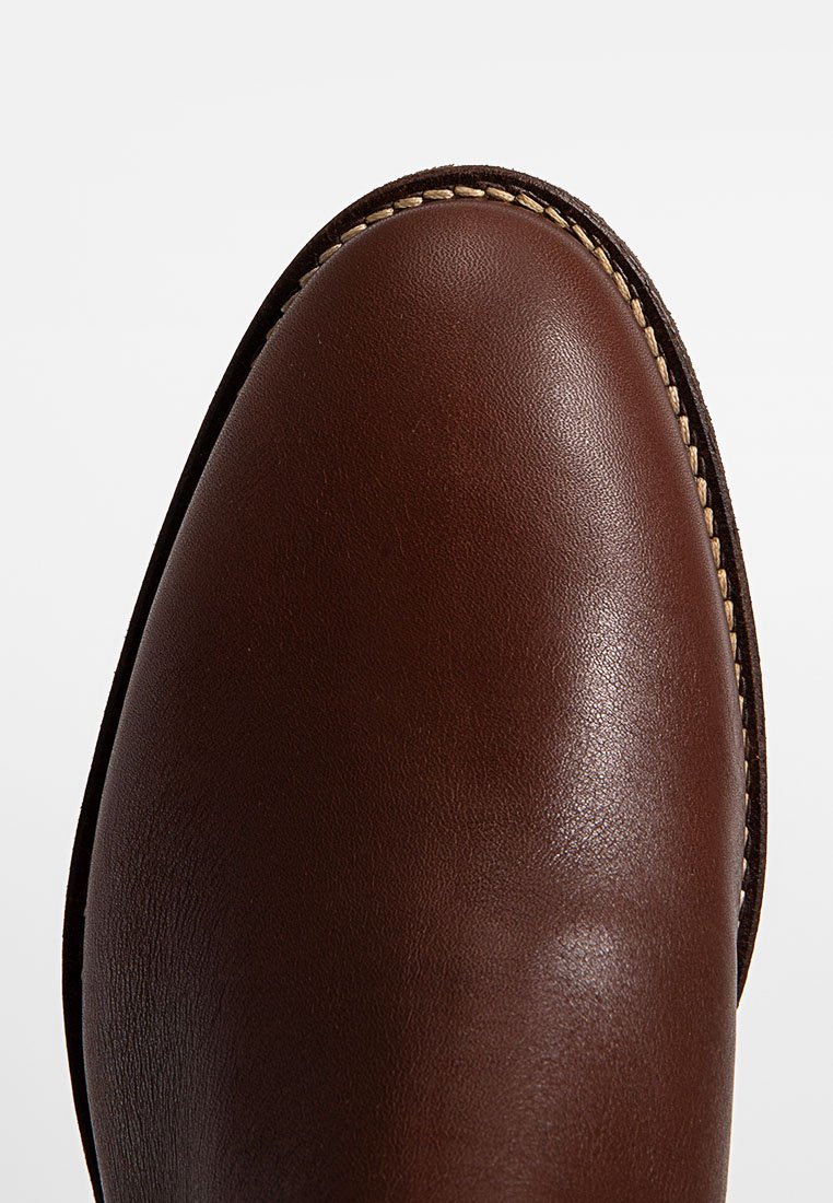 Braune Leder-Schuh mit glatter Oberfläche, runder Zehenpartie und kontrastierender Naht am Rand. Einfaches Design ohne auffällige Muster.