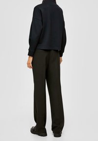 Sudadera negra corta con cuello alto, combinada con pantalones negros de corte holgado y botas negras gruesas. Tejido suave y diseño minimalista.