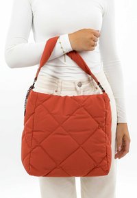 Quilted orange handbag with a soft texture, a wide strap, and chain details. The design features a spacious structure and a rectangular shape.