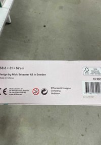 Kartongförpackning som mäter 58,6 x 31 x 52 cm, med text, logotyper och säkerhetssymboler i svart på en ljusrosa bakgrund.