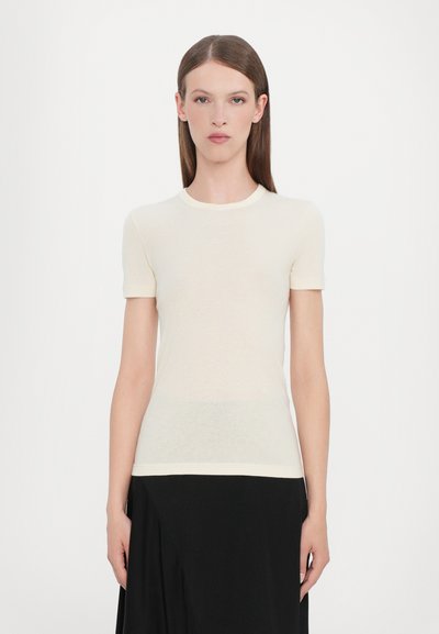 T-shirt clair en crème à manches courtes fabriqué en tissu doux et léger avec un col arrondi et un léger logo près de l'ourlet.