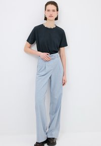 Zwarte T-shirt, lichtgewicht stof, ronde halslijn. Lichtblauwe broek, high-waisted, riem, geplooide voorkant, wijde pijpen, gestructureerde stof, zwarte schoenen.