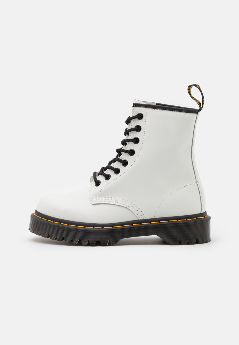 Botte de combat en cuir blanc à lacets, semelle noire, surpiqûres jaunes, languette et semelle crantée sur fond uni.
