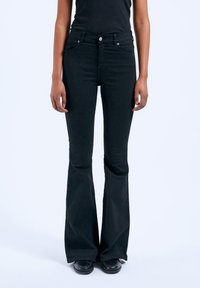 Black flared jeans with a high waistband, front and back pockets, and a smooth fabric texture. Features a front button and zipper closure.