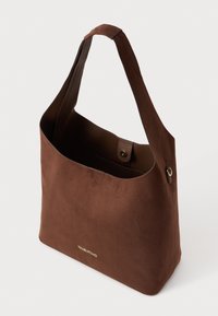 Καφέ σουέτ τσάντα hobo με μία ενιαία λουρί, διαθέτει μαγνητική κούμπωμα και χρυσό λογότυπο μπροστά. Λείο, υφασμένο επιφάνεια.