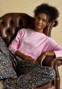 Pink long-sleeve shirt paired with dark floral-patterned pants. The model is seated on a brown leather tufted armchair.