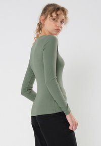 Maglietta a maniche lunghe, a costine, di colore verde oliva con una silhouette aderente. Il retro presenta un collo arrotondato, un tessuto testurizzato e una finitura liscia.