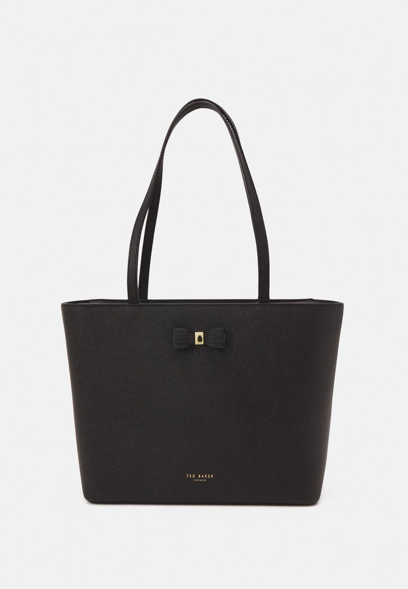Sac cabas en cuir noir avec double bandoulière, petit nœud décoratif avec accent doré et logo "Ted Baker London" en or au centre en bas.