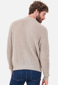 Beiger gestrickter Pullover mit strukturiertem Muster, rundem Ausschnitt sowie gerippten Bündchen und Saum, getragen über dunkelblauer Jeans.