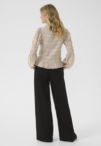 Blusa beige con arricciature, maniche a sbuffo e orlo smerlato, abbinata a pantaloni neri larghi. Tessuto liscio e dettagli del corpino aderente visibili.