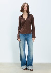 Brown satin button-up shirt with a collar and long sleeves, paired with light blue flared jeans featuring a denim hem detail.