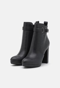 Bottes noires à la cheville en cuir lisse, talons hauts carrés, fermeture éclair latérale et une sangle avec une boucle en métal en accent.