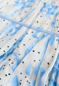 Ľahké šaty z tkaniny s modrými listovými vzormi na bielom pozadí, doplnené malými čiernymi bodkami a modrou saténovou stuhou.