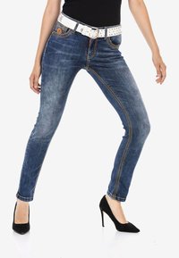 Dünne blaue Jeans aus Denim, mit orangefarbenen Nähten, einem weißen, mit Nieten besetzten Gürtel und einer mittelhohen Taille. Mit vorderen Taschen akzentuiert.