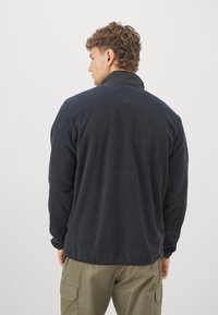 Marine fleecejakke med lange ærmer og høj krave. Stoffet ser blødt og struktureret ud, og designet er strømlinet uden mønstre.