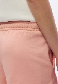 Pantalon de survêtement rose avec une texture douce, une ceinture élastique, des poches latérales et une coupe décontractée, assorti à un haut de couleur claire.